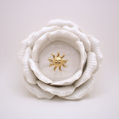 White ceramic flower with a gold sun emblem on a light gray background