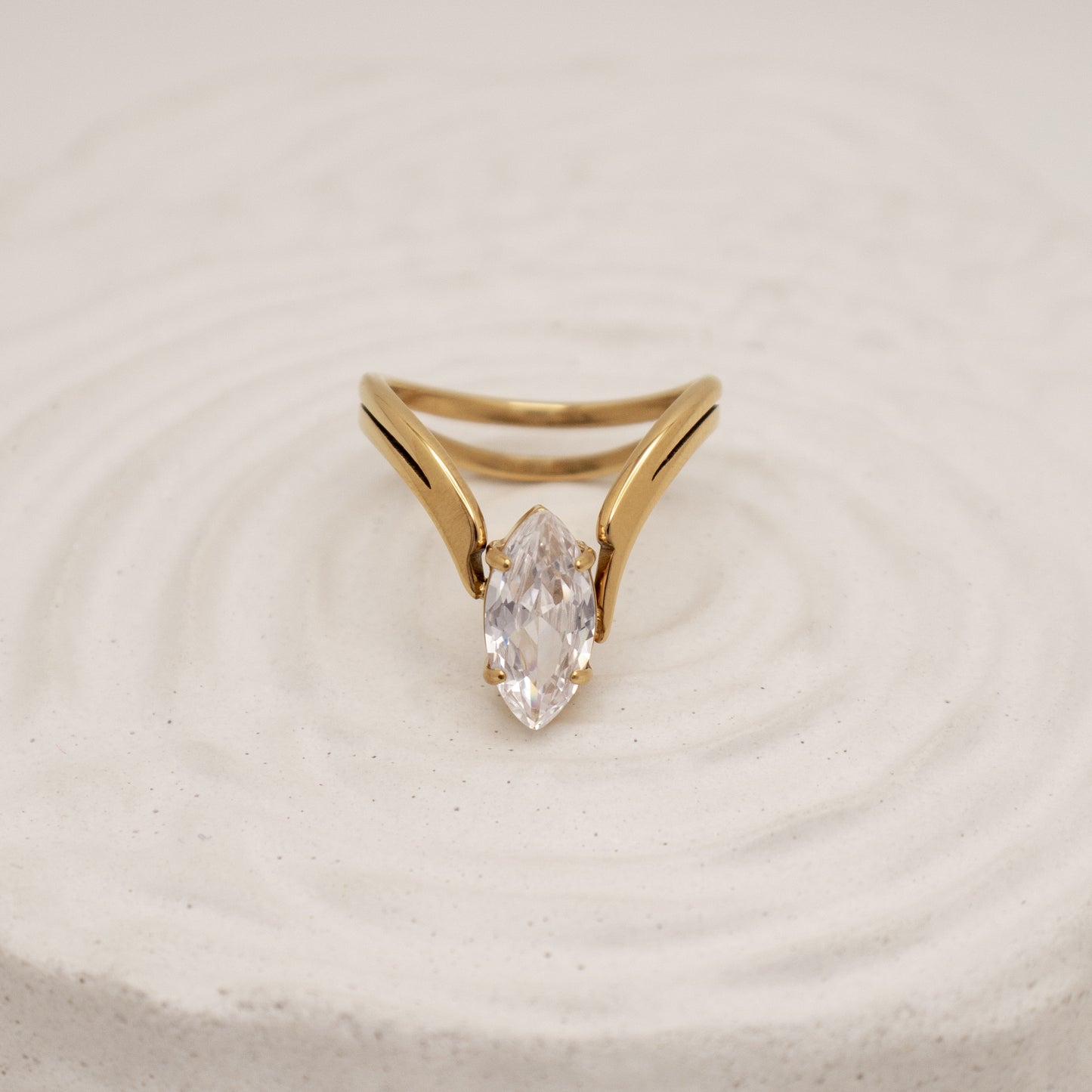 Gold ring with a clear gemstone on a beige background