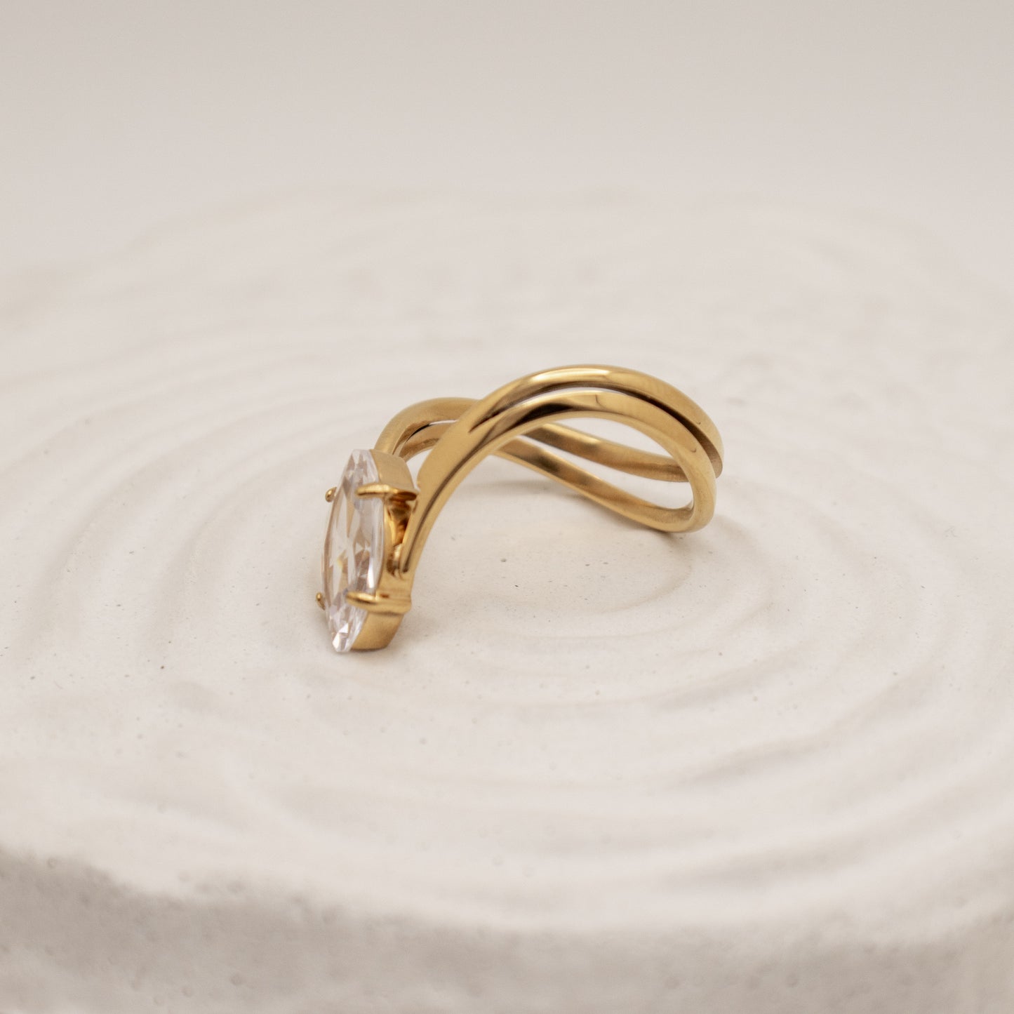 Gold ring with a clear gemstone on a beige background
