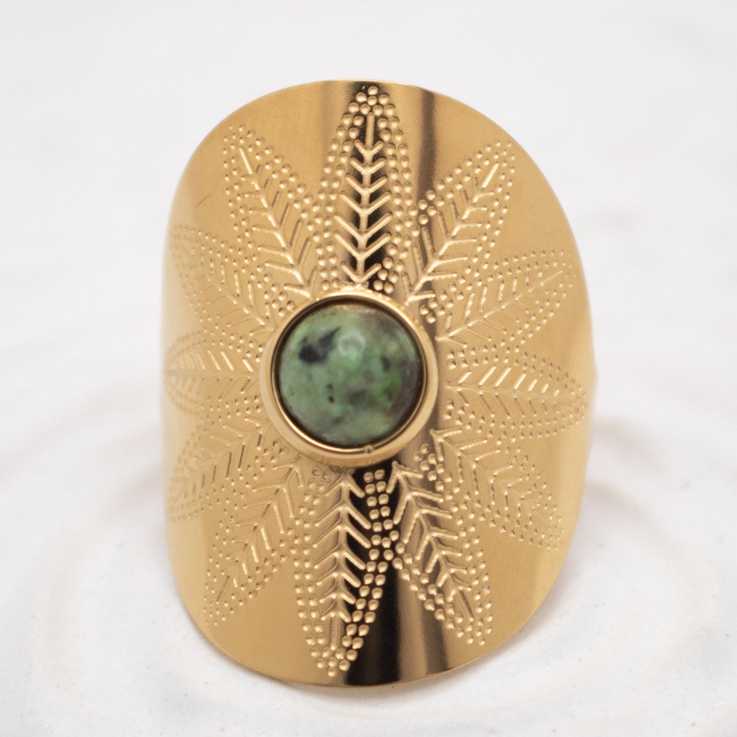 Gold decorative object with a central green stone on a white background