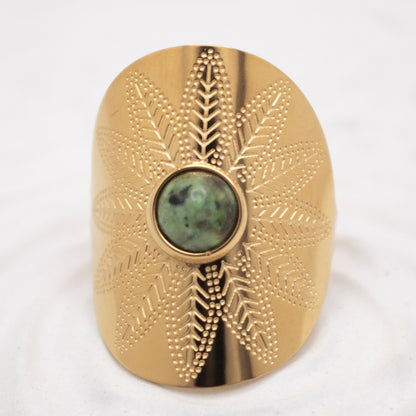 Gold decorative object with a central green stone on a white background