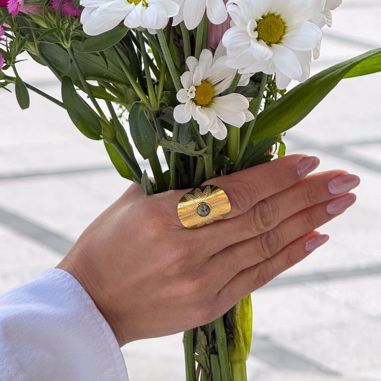 Hand wearing a gold ring with a green gemstone, holding a bouquet of flowers.