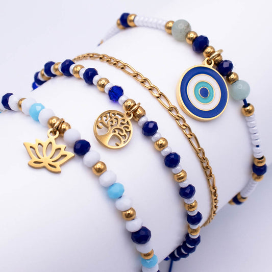 A set of three beaded and chain bracelets displayed on a white mannequin arm. The bracelets feature dark blue, white, and light blue beads, gold spacer beads, and gold-toned metal charms including a tree of life medallion, a lotus flower charm, and a blue and white evil eye circle charm.