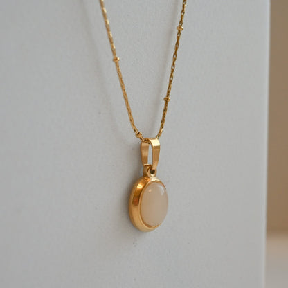 Gold necklace with a round pendant on a light gray background