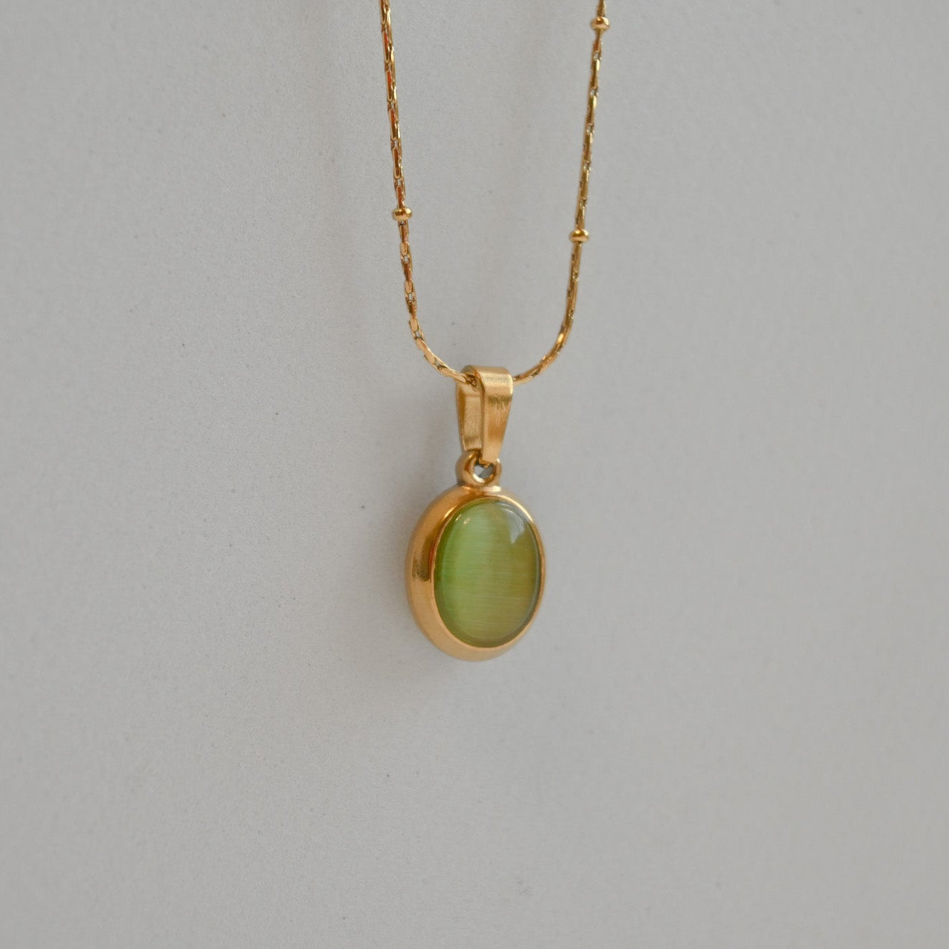 Gold necklace with a green pendant on a gray background