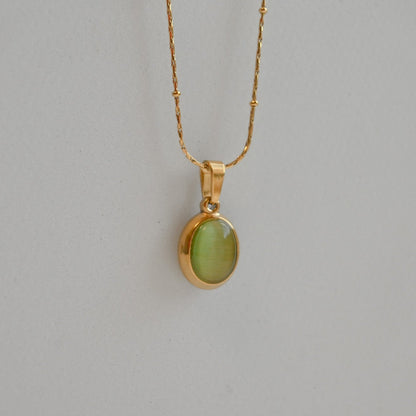 Gold necklace with a green pendant on a gray background