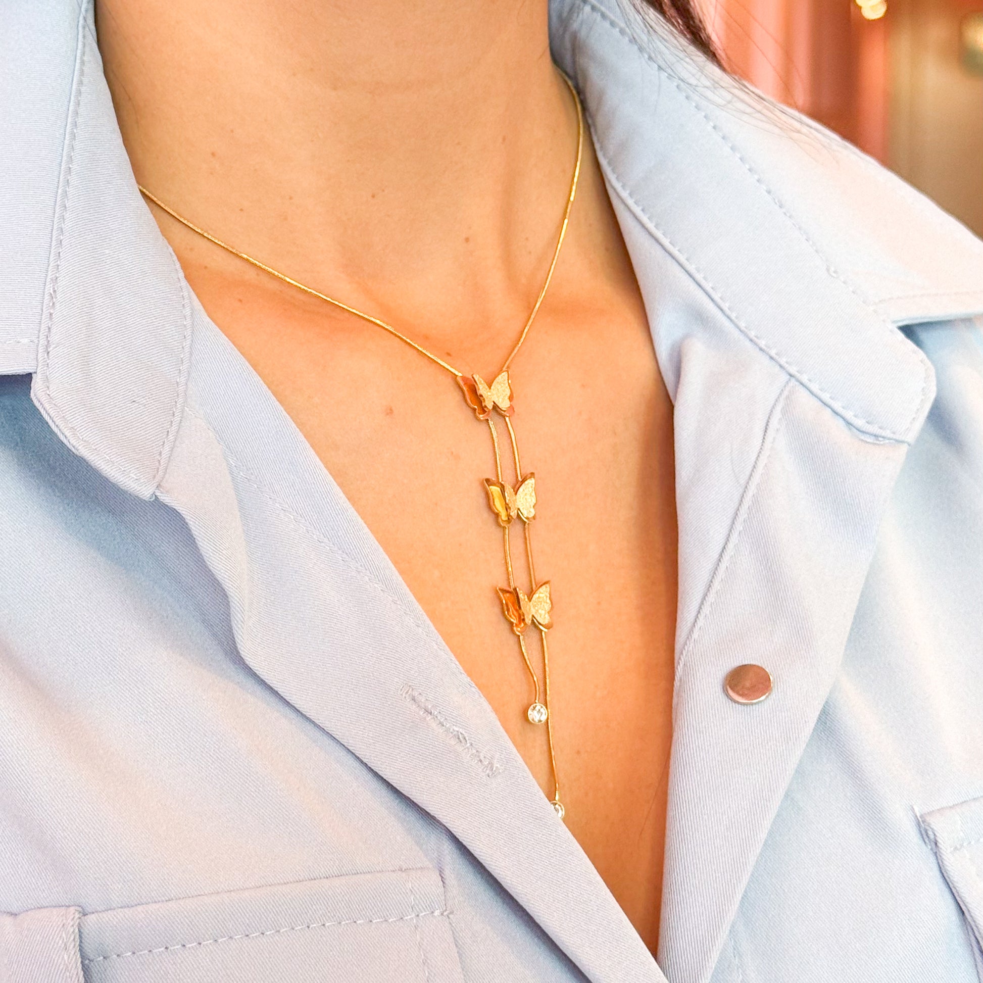 Gold butterfly necklace worn by a person with a light blue shirt.