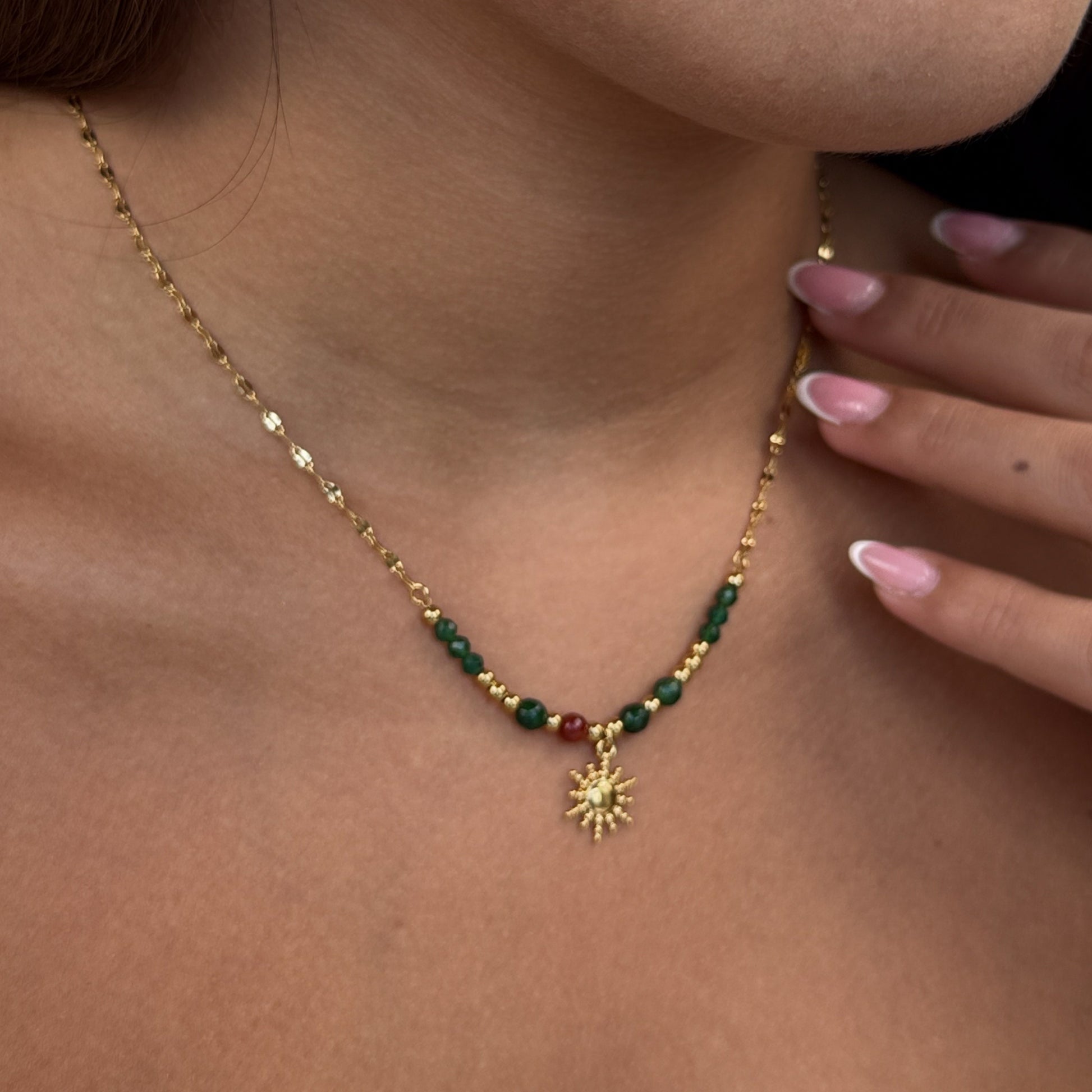 Gold necklace with green beads and a sun pendant on a person's neck.