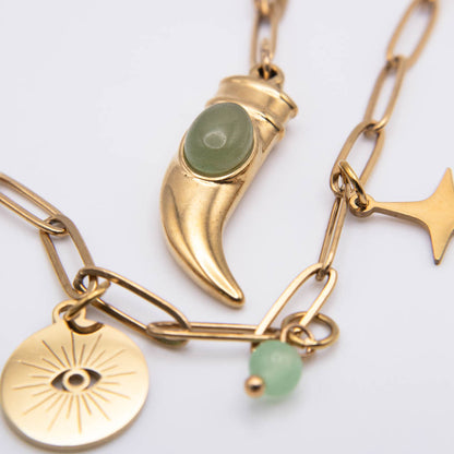 Gold-toned charm necklace featuring a crescent moon pendant with a green stone, a gold disc charm with an eye design, and a small green bead, shown on a white background.