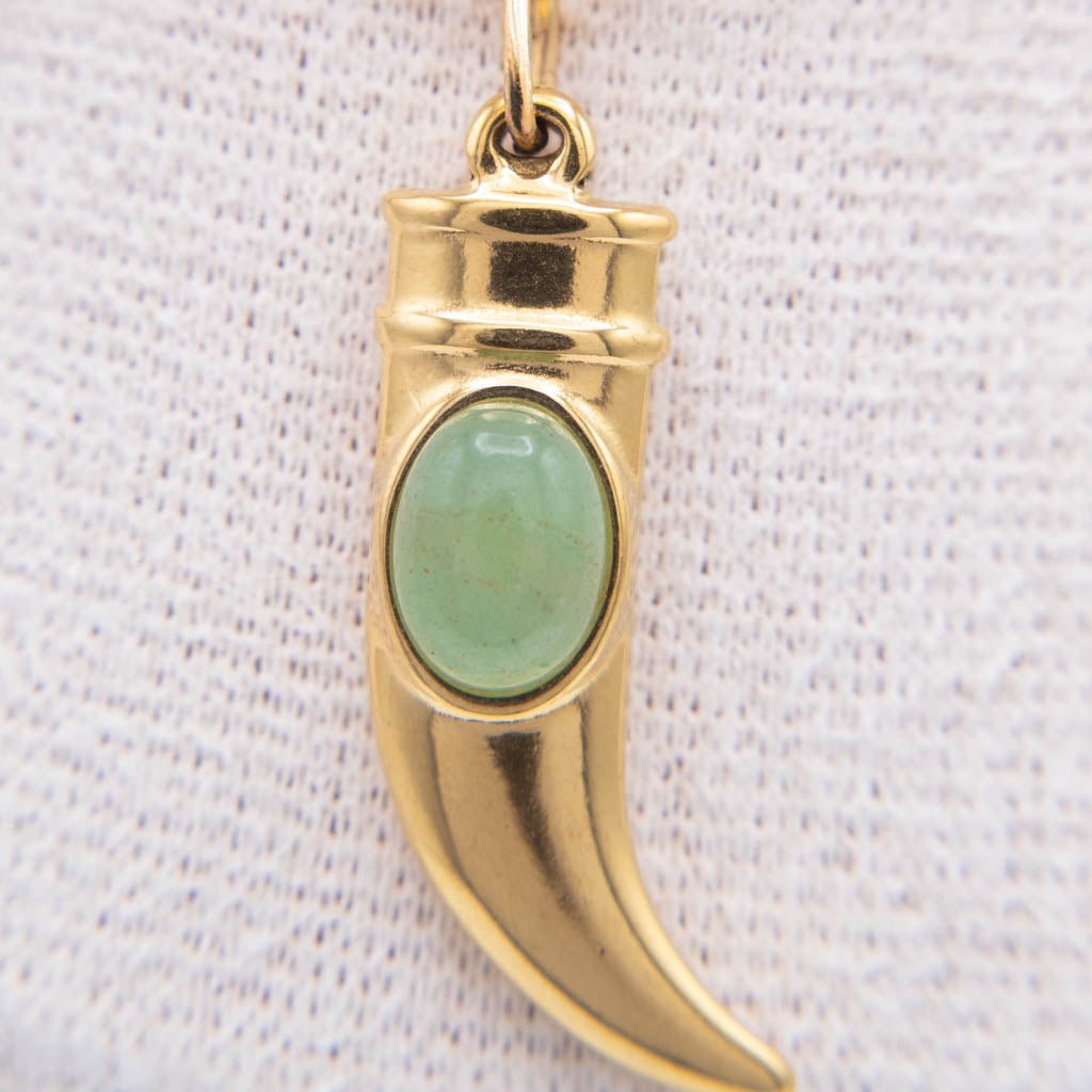 A gold crescent-shaped pendant charm featuring an oval green stone inlay, displayed against a textured white fabric background.
