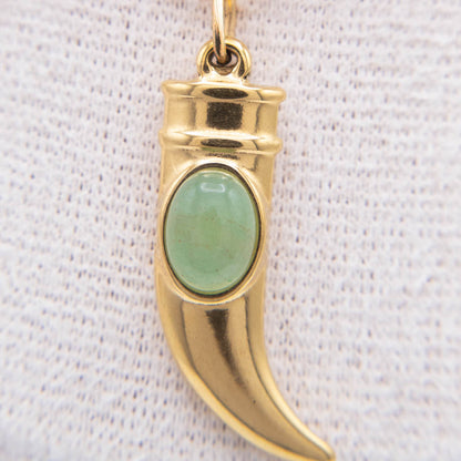 A gold crescent-shaped pendant charm featuring an oval green stone inlay, displayed against a textured white fabric background.