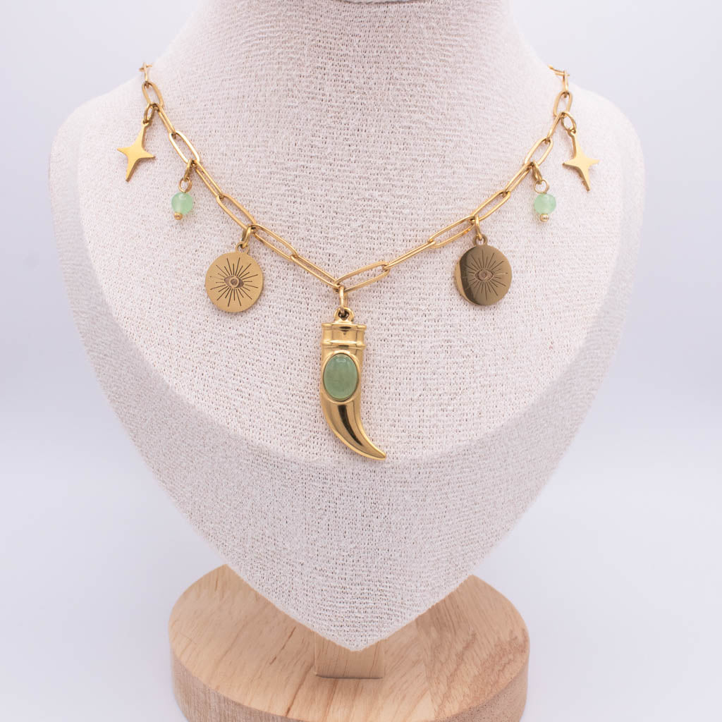 A gold-toned chain necklace displayed on a cream fabric mannequin bust. The necklace features multiple charms, including three gold stars, two textured gold discs, a central gold crescent moon pendant with a light green stone, and small light green bead accents.