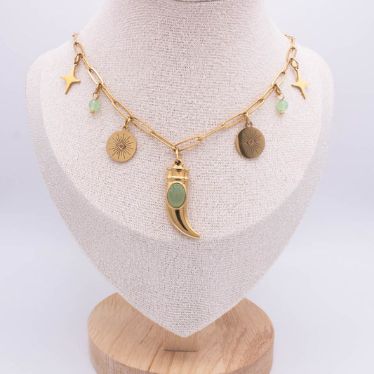 A gold-toned chain necklace displayed on a cream fabric mannequin bust. The necklace features multiple charms, including three gold stars, two textured gold discs, a central gold crescent moon pendant with a light green stone, and small light green bead accents.