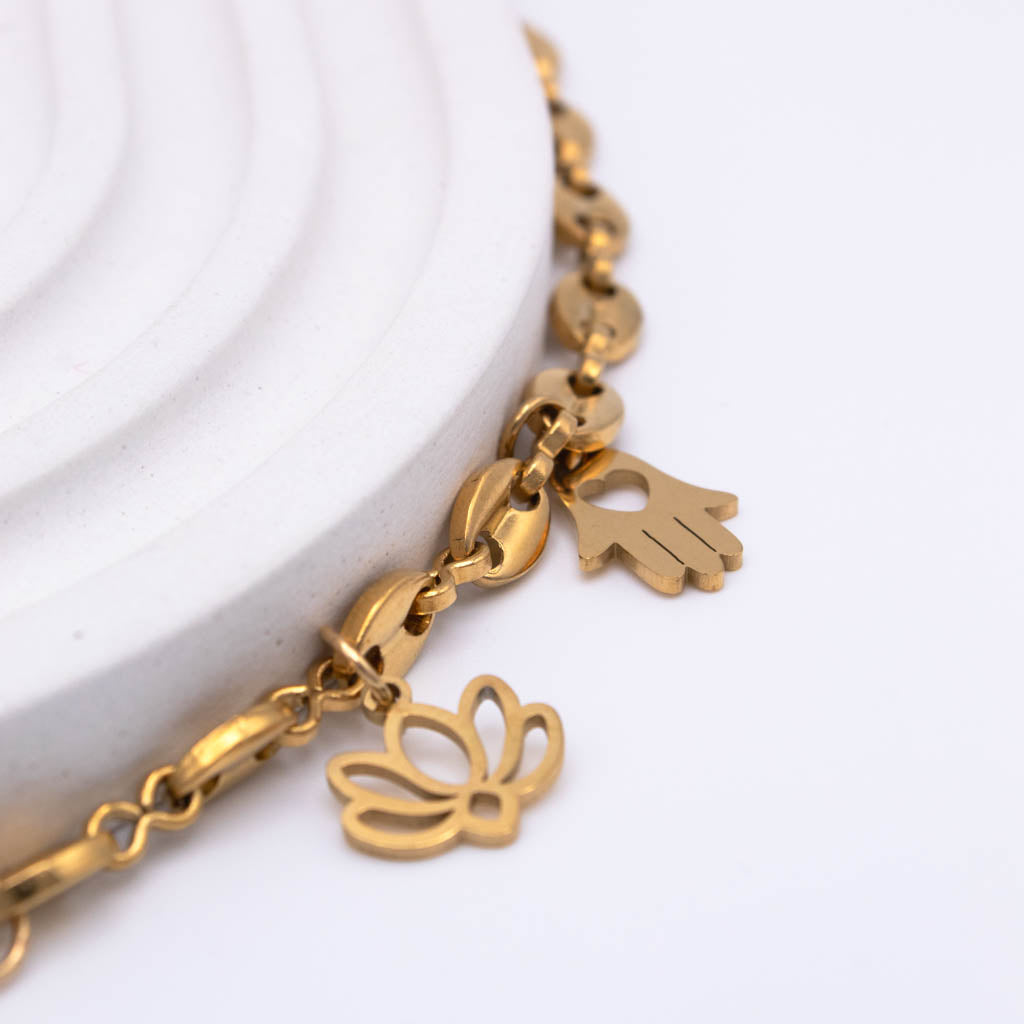 A gold-tone charm bracelet with a butterfly and hand charms, displayed on a white textured ceramic riser against a clean white background.