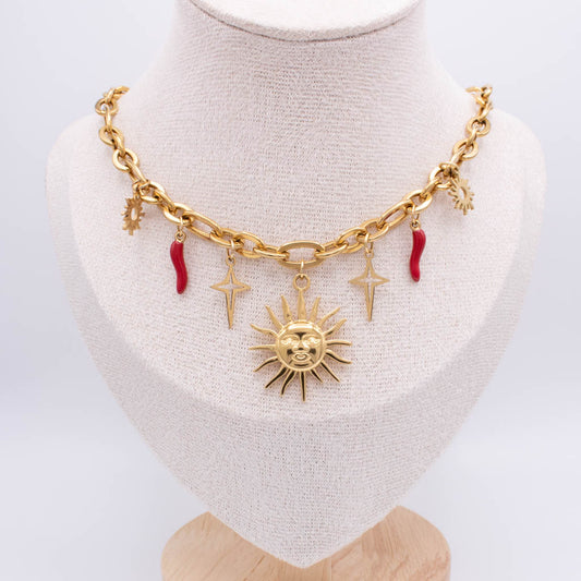 A gold-tone chunky chain necklace displayed on a cream fabric mannequin bust. The necklace features a central sun face charm, two lightning bolt charms, a small crescent moon charm, and two small red italian horns charms.