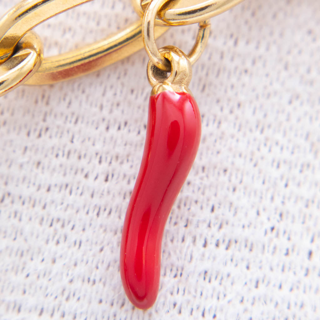 A close-up of a glossy red italian horn charm hanging from a gold-tone chain on a textured white fabric background.