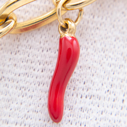 A close-up of a glossy red italian horn charm hanging from a gold-tone chain on a textured white fabric background.