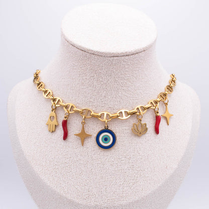 Gold-tone charm necklace displayed on a cream fabric jewelry bust. The necklace features a heart-link chain with multiple dangling charms, including a blue and white evil eye, gold stars, a hamsa hand, a lotus flower, and small red italian horn.