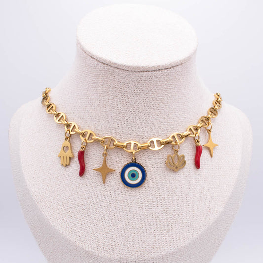 Gold-tone charm necklace displayed on a cream fabric jewelry bust. The necklace features a heart-link chain with multiple dangling charms, including a blue and white evil eye, gold stars, a hamsa hand, a lotus flower, and small red italian horn.