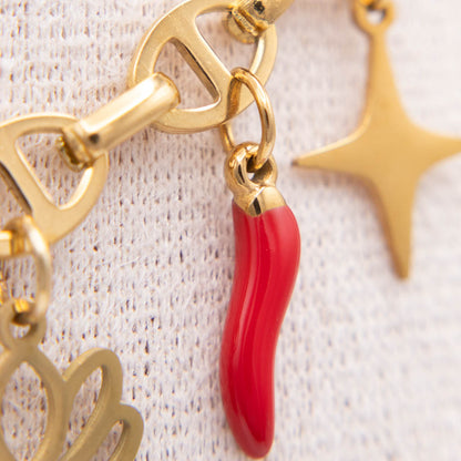 Gold-tone charm bracelet featuring a glossy red italian horn charm and a gold star charm, displayed on a textured white fabric background.