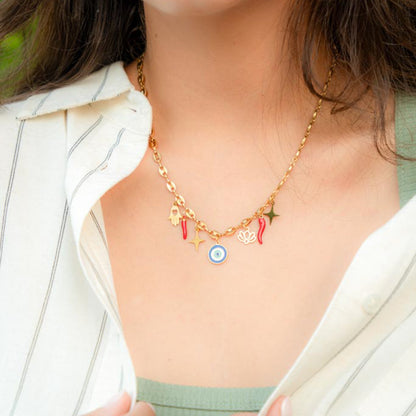 A close-up of a gold chain necklace with multiple charms, including a blue and white evil eye pendant, worn by a person in a white collared shirt.