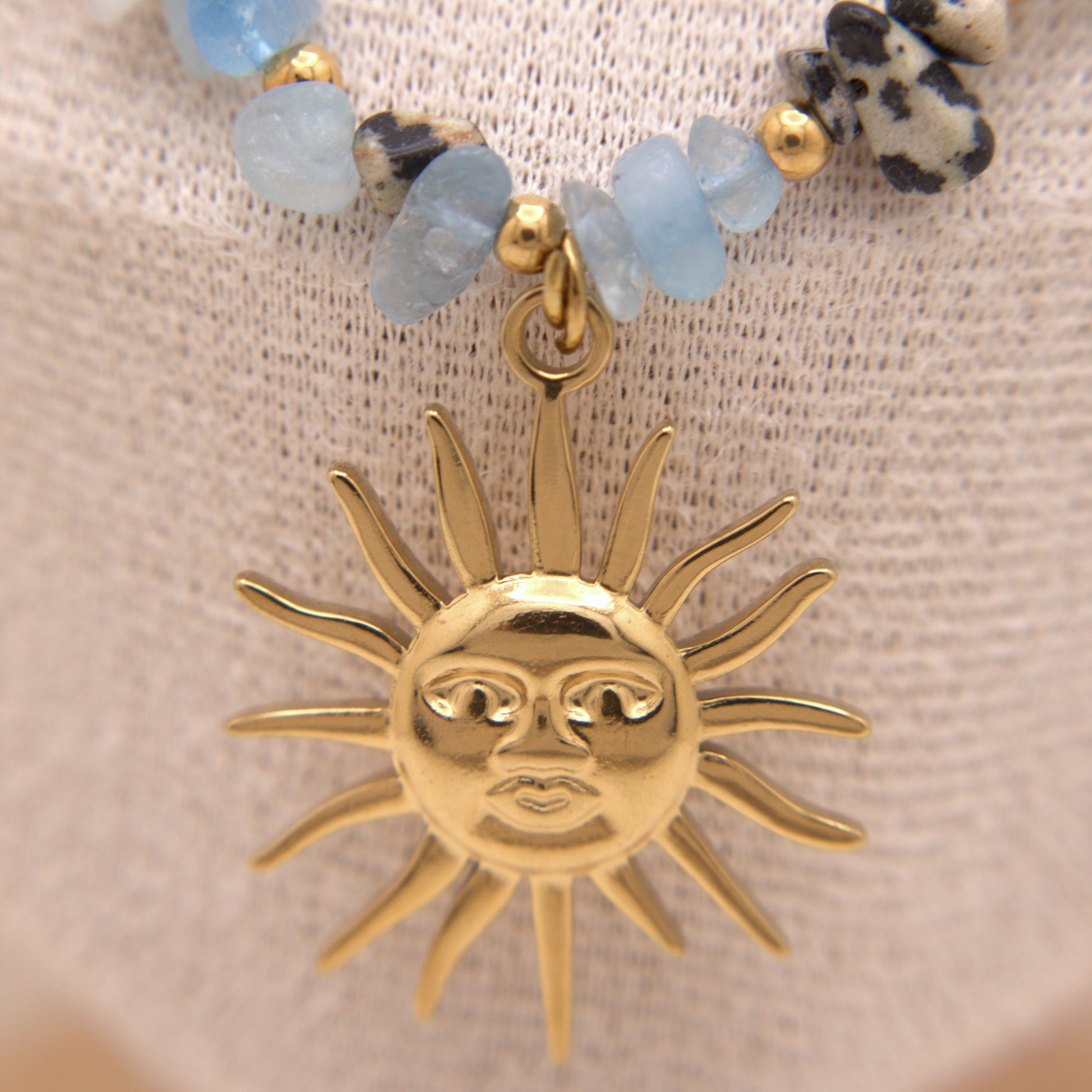Gold sun pendant on a beaded bracelet with a beige background