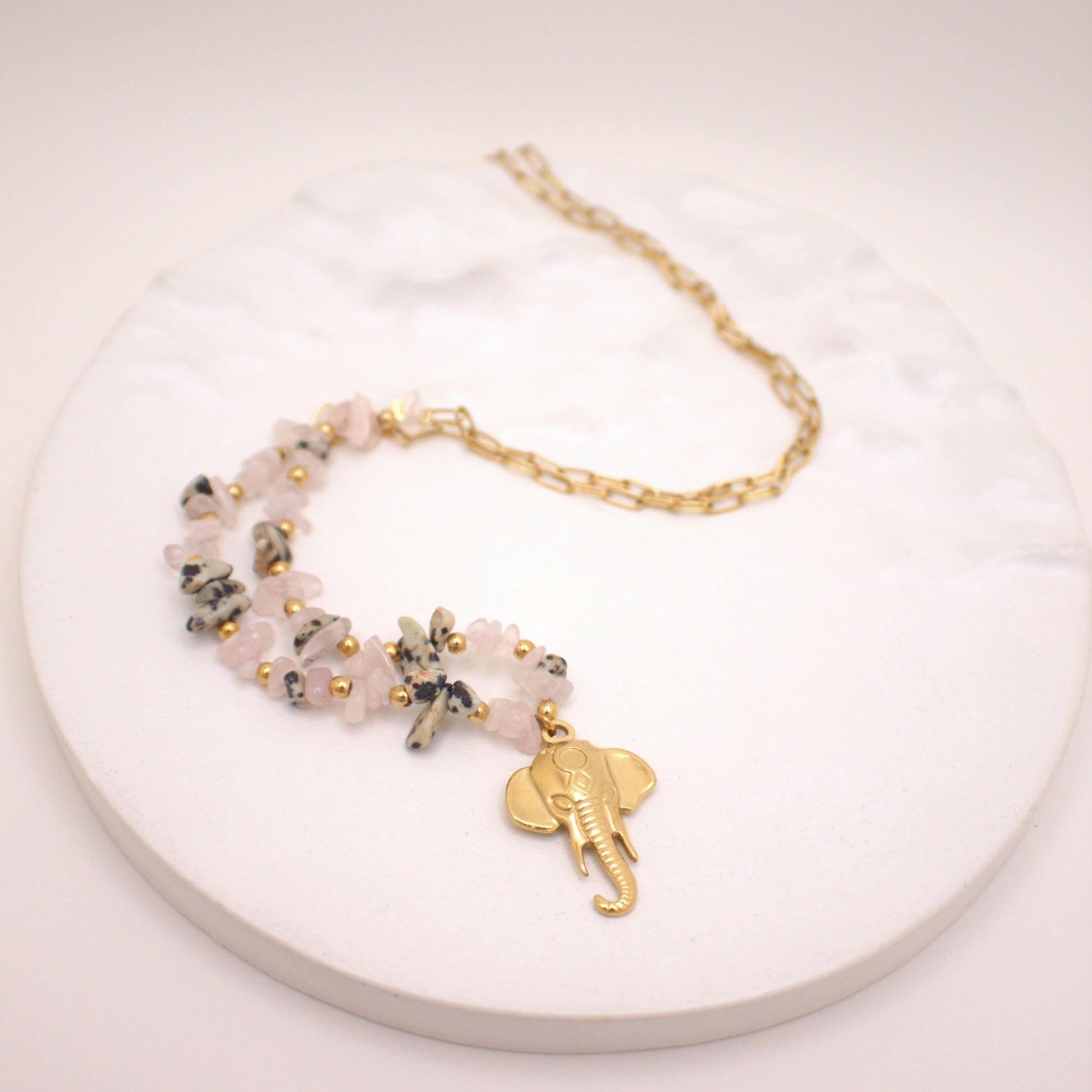 Bracelet with pink beads and gold elephant charm on a white plate