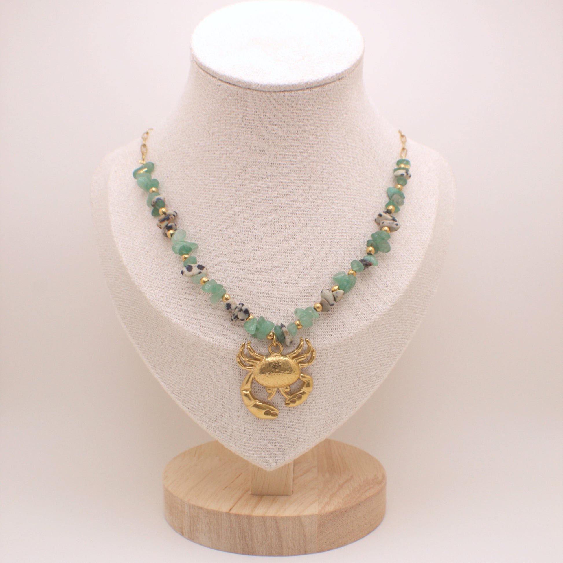 Necklace with green beads and gold crab pendant on a white mannequin bust.