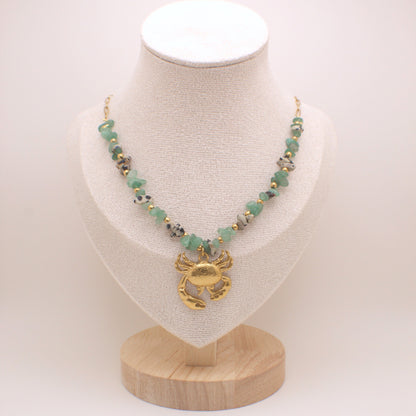 Necklace with green beads and gold crab pendant on a white mannequin bust.