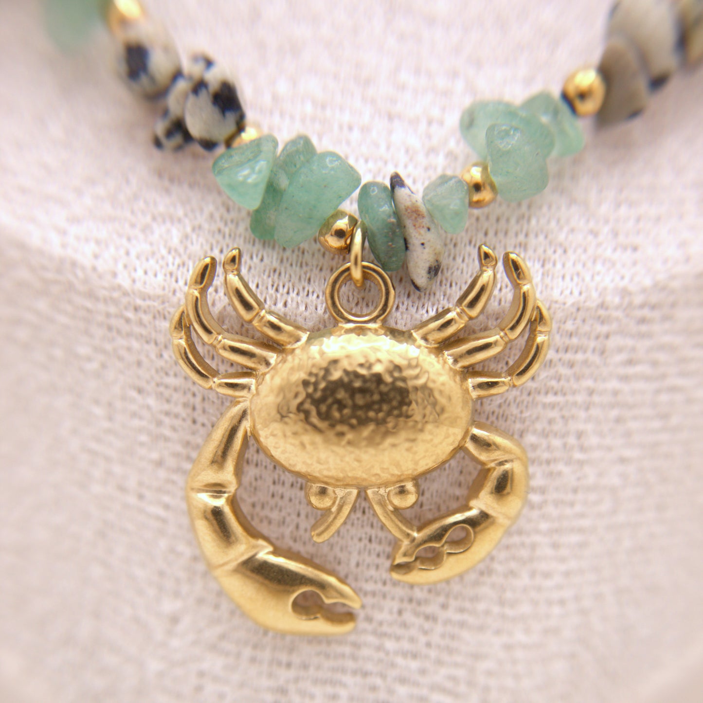 Gold crab pendant on a beaded necklace with a textured fabric background