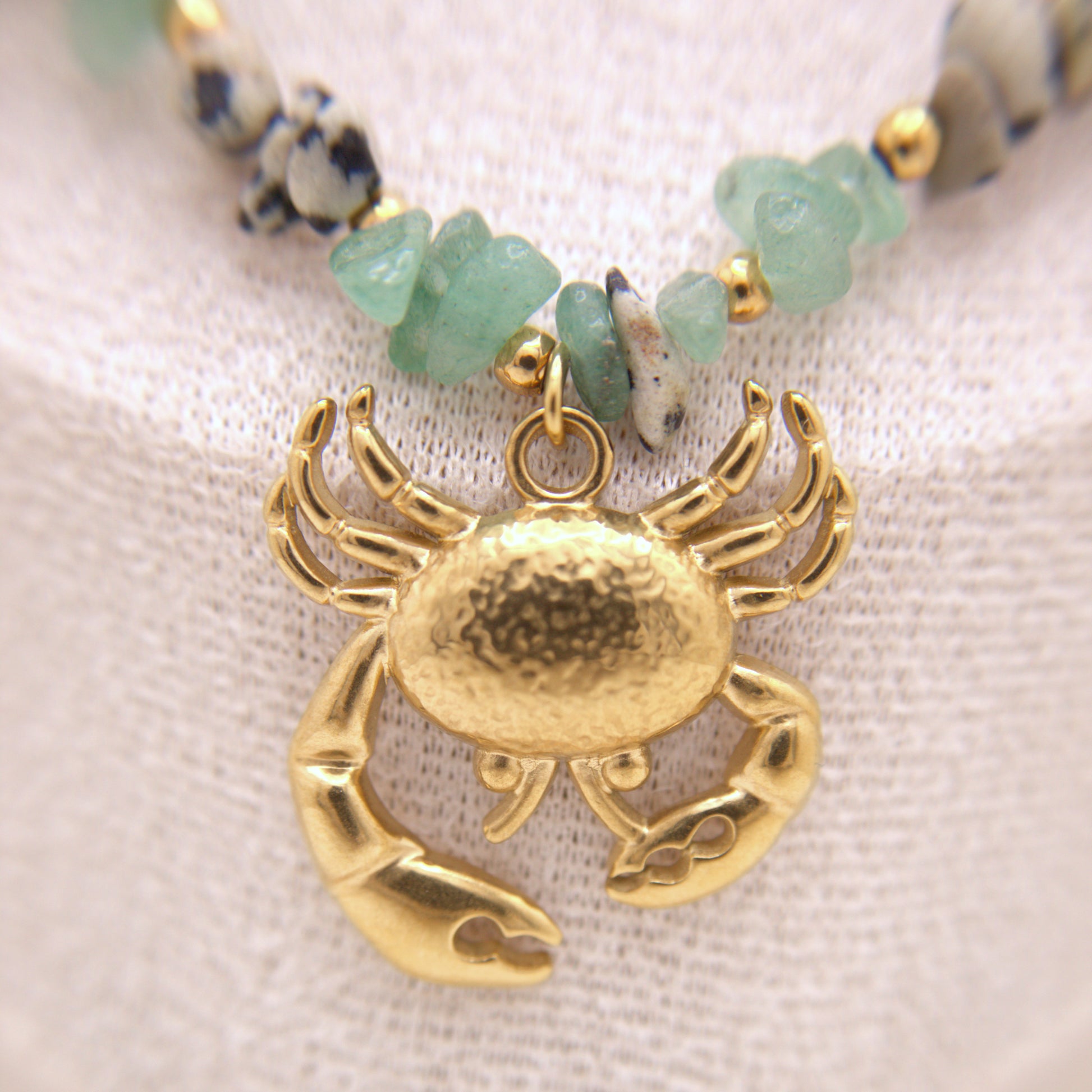Gold crab pendant on a beaded necklace with a textured fabric background