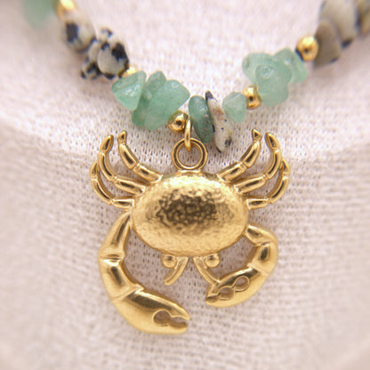 Gold crab pendant on a beaded necklace with a textured fabric background