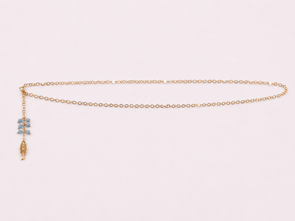 A delicate gold chain necklace with a small blue and gold charm, displayed on a light pink background.
