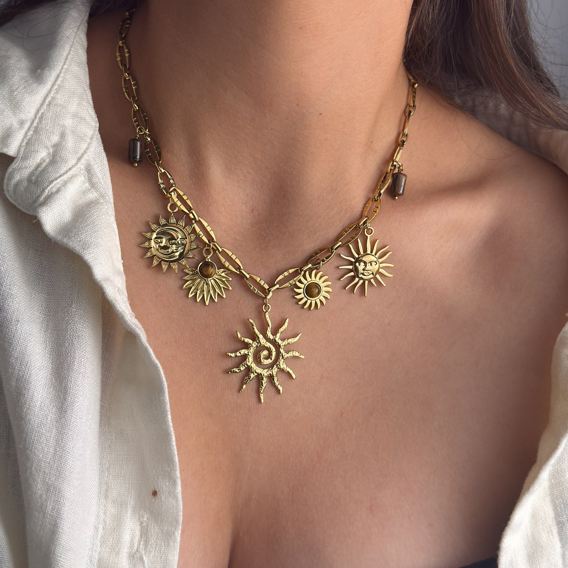 Gold sun-shaped necklace on a person wearing a white shirt