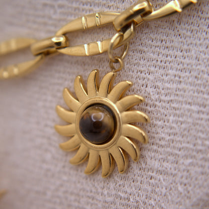 Gold sun-shaped pendant with a central brown gemstone on a beige fabric background