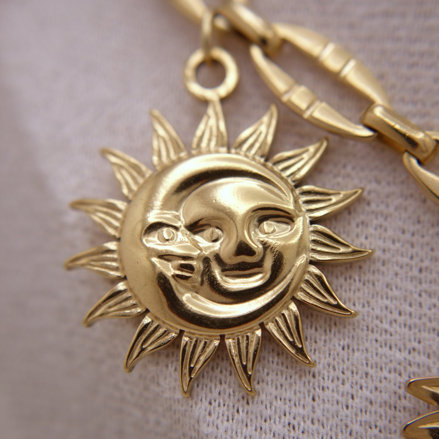 Gold sun and moon pendant on a chain against a light fabric background