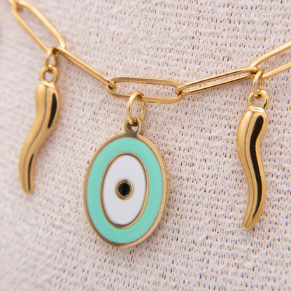 Gold-tone chain necklace with an oval evil eye pendant in mint green, white, and black, flanked by two small wavy gold charms, displayed on a textured cream fabric.