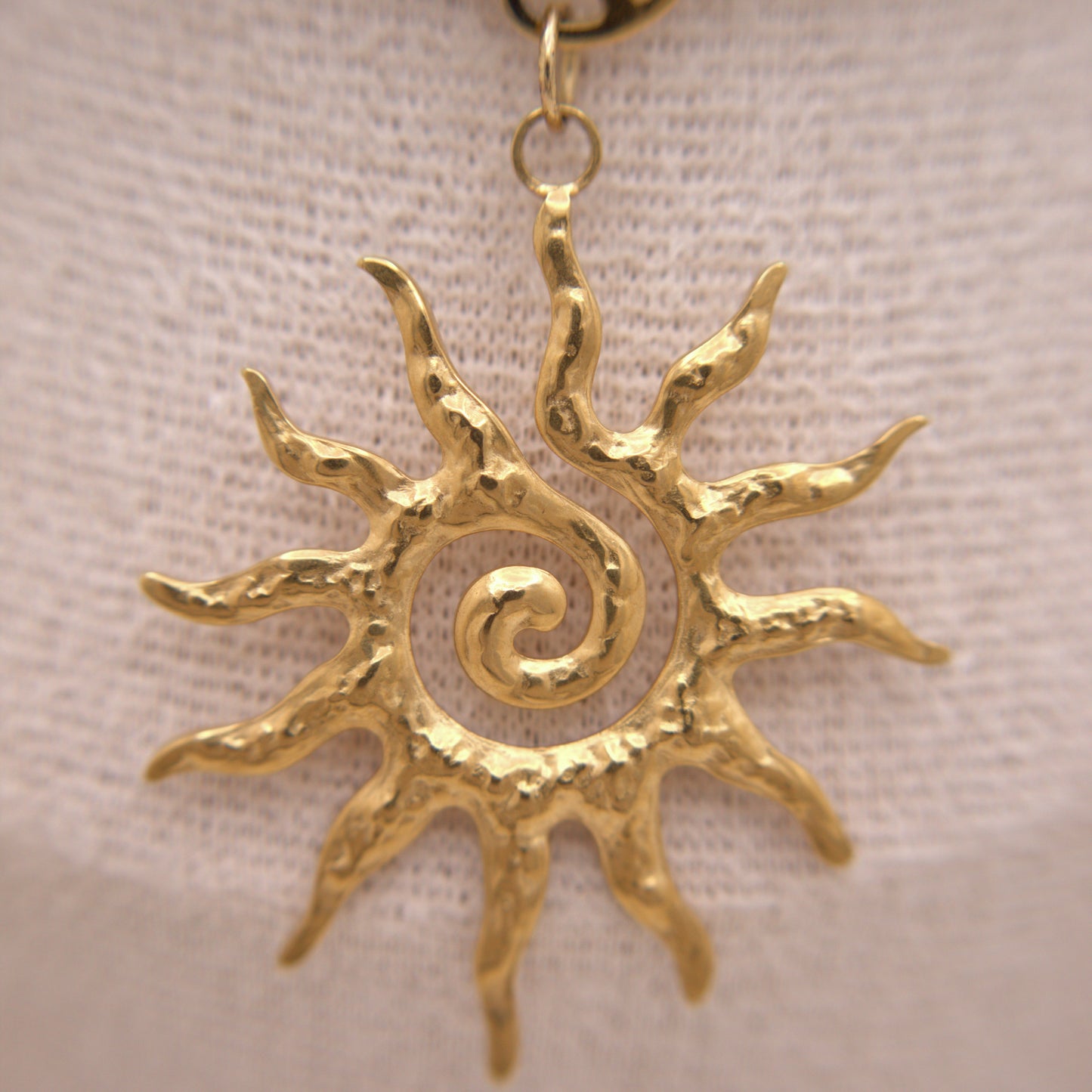 Gold sun-shaped pendant on a beige fabric background