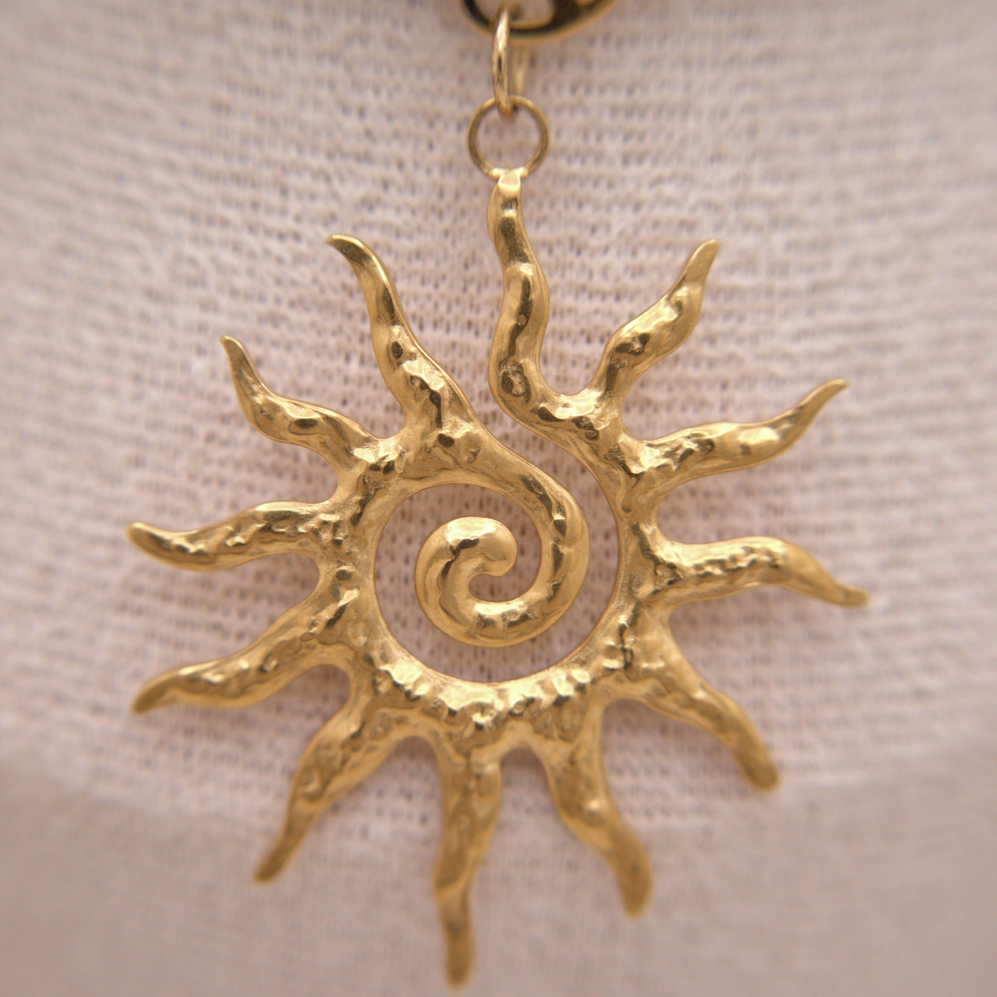 Gold sun-shaped pendant on a beige fabric background