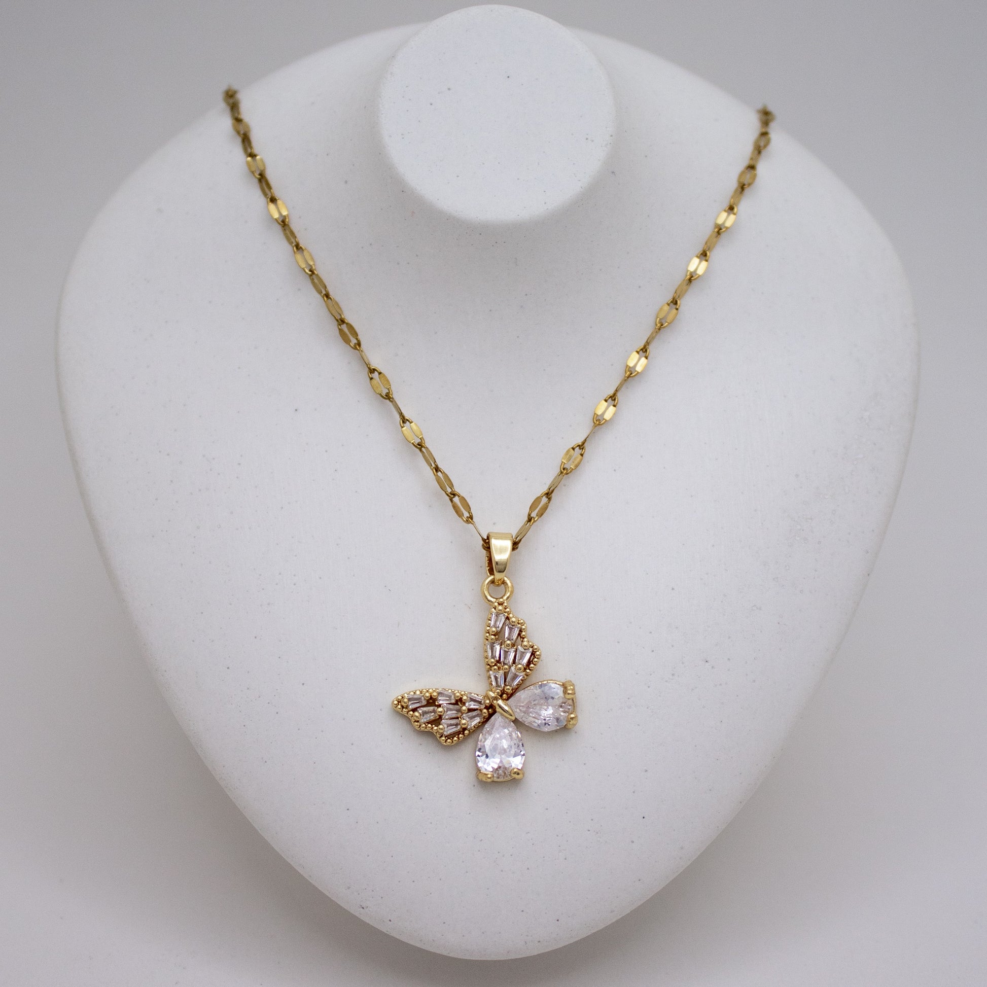 Gold necklace with a butterfly pendant on a white stand