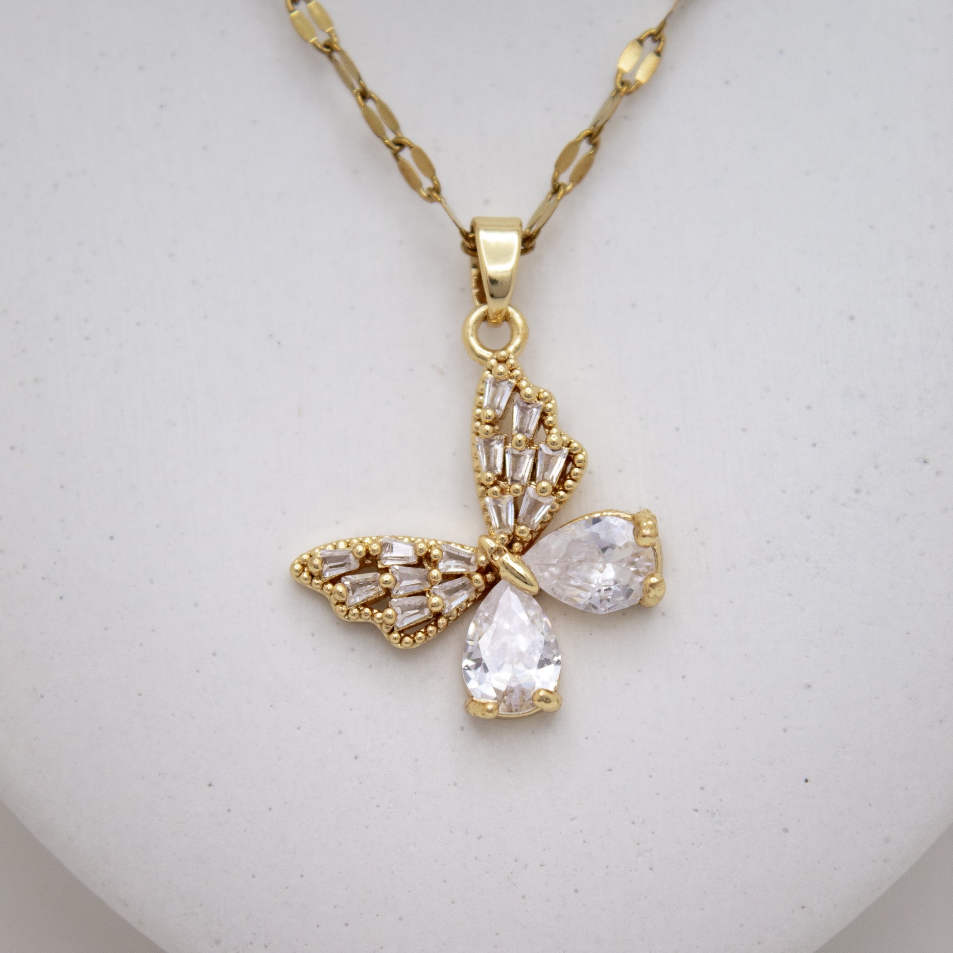 Gold butterfly-shaped pendant necklace on a light gray background