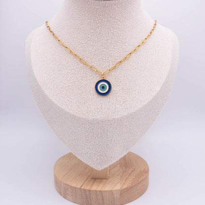 A gold chain necklace with a circular evil eye pendant, displayed on a textured cream fabric jewelry bust mounted on a wooden stand against a light gray background.