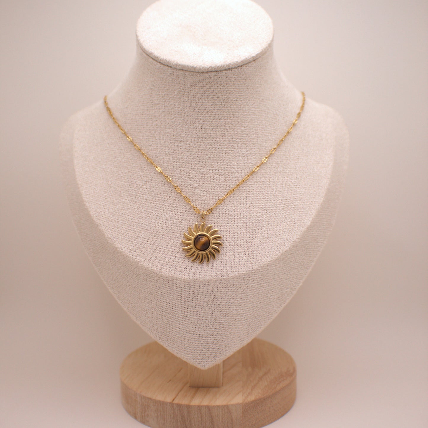 Gold necklace with a sunflower pendant on a mannequin bust against a white background