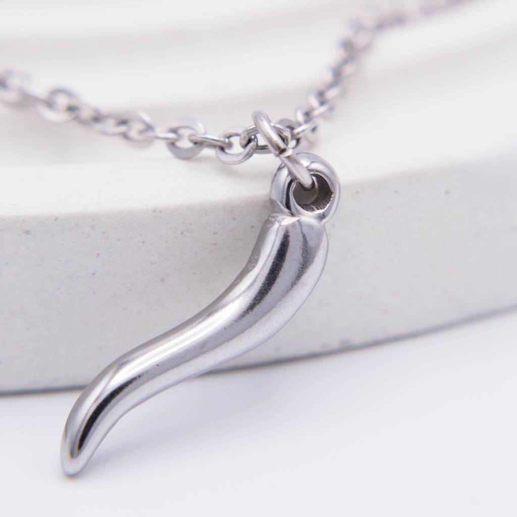 A silver-toned metal pendant necklace featuring a curved, stylized shape, shown on a white textured surface with a matching chain.