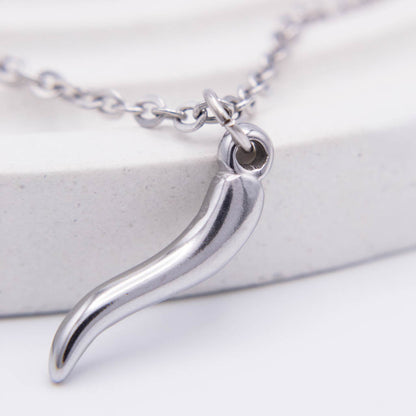 A silver-toned metal pendant necklace featuring a curved, stylized shape, shown on a white textured surface with a matching chain.