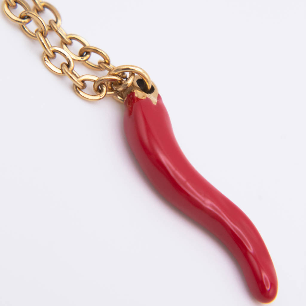A close-up of a gold-tone chain necklace with a glossy red italian horn-shaped pendant on a plain white background.