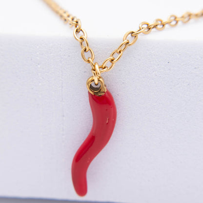 A gold chain necklace featuring a glossy red italian horn pendant, displayed on a textured white surface.