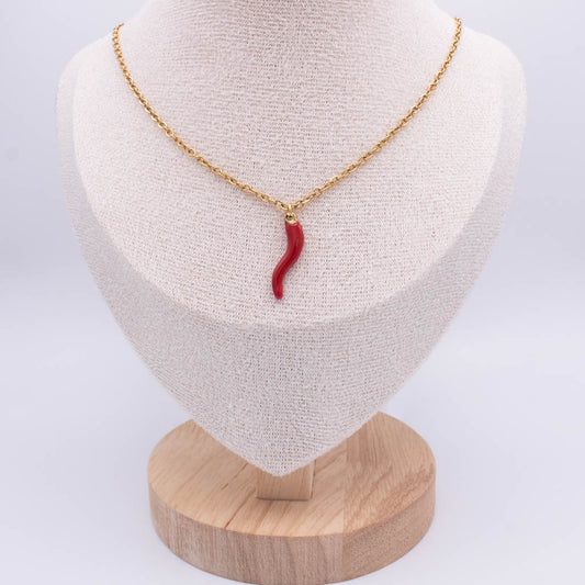 A gold chain necklace with a curved red pendant displayed on a cream fabric jewelry bust mounted on a round wooden base, photographed against a light gray background.