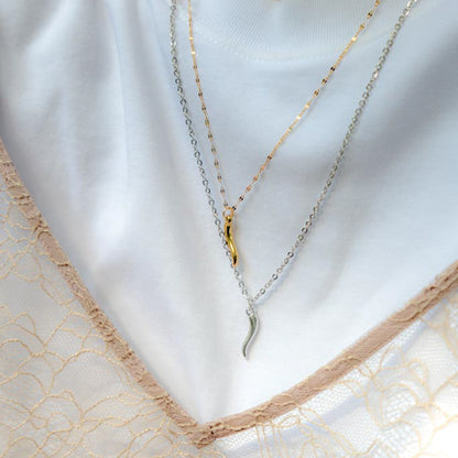 Two layered necklaces displayed on a white mannequin bust: one with a gold chain and leaf-shaped pendant, and one with a silver chain and silver leaf-shaped pendant, styled over a white top with beige lace trim.