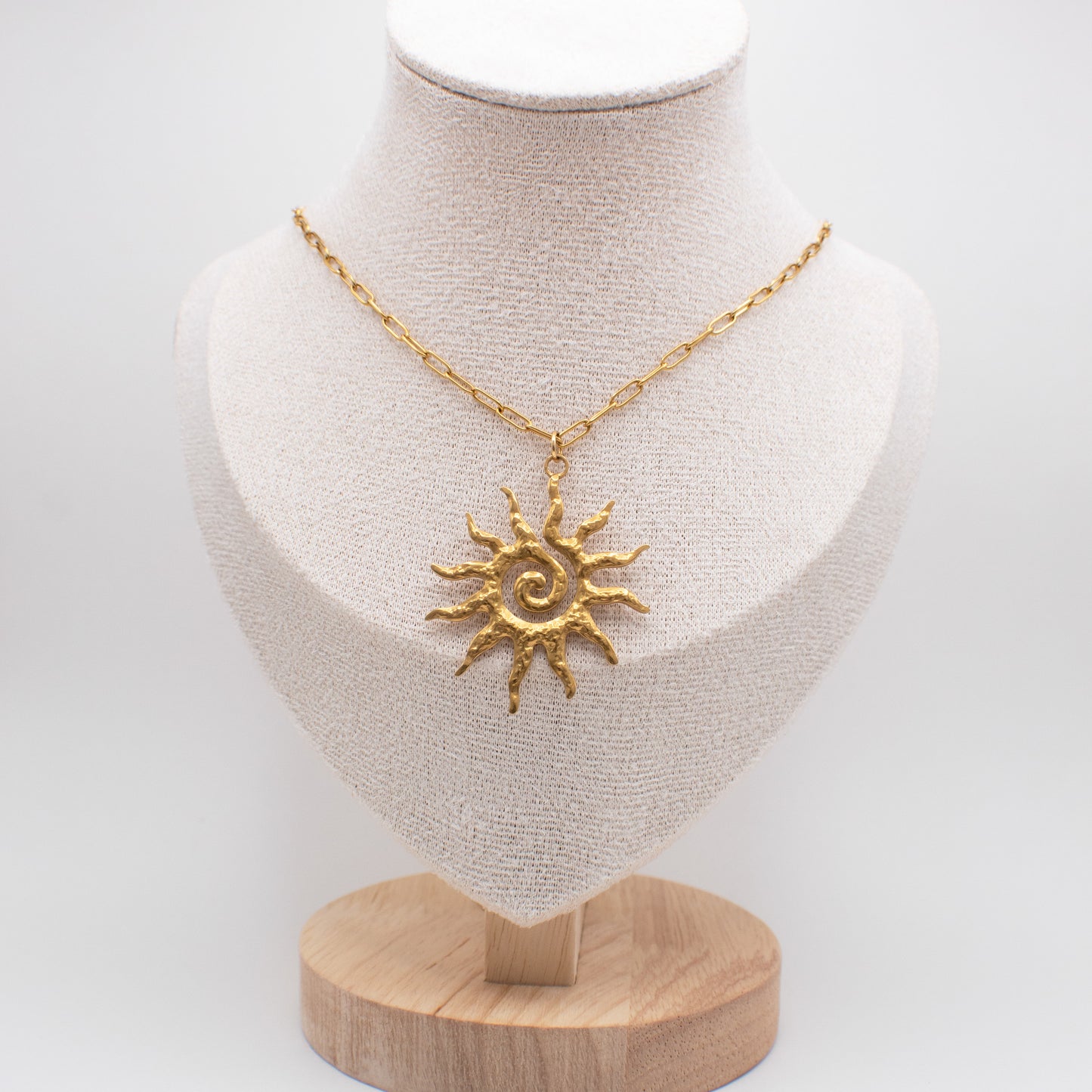 Gold sun-shaped pendant necklace on a mannequin bust with a white background